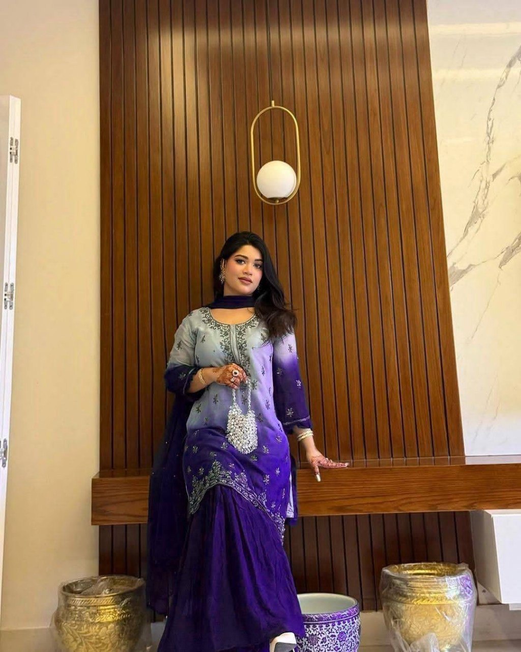 Woman in a purple and gray traditional outfit standing indoors against a wooden wall.