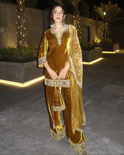 Woman in a gold velvet traditional outfit standing outdoors at night.