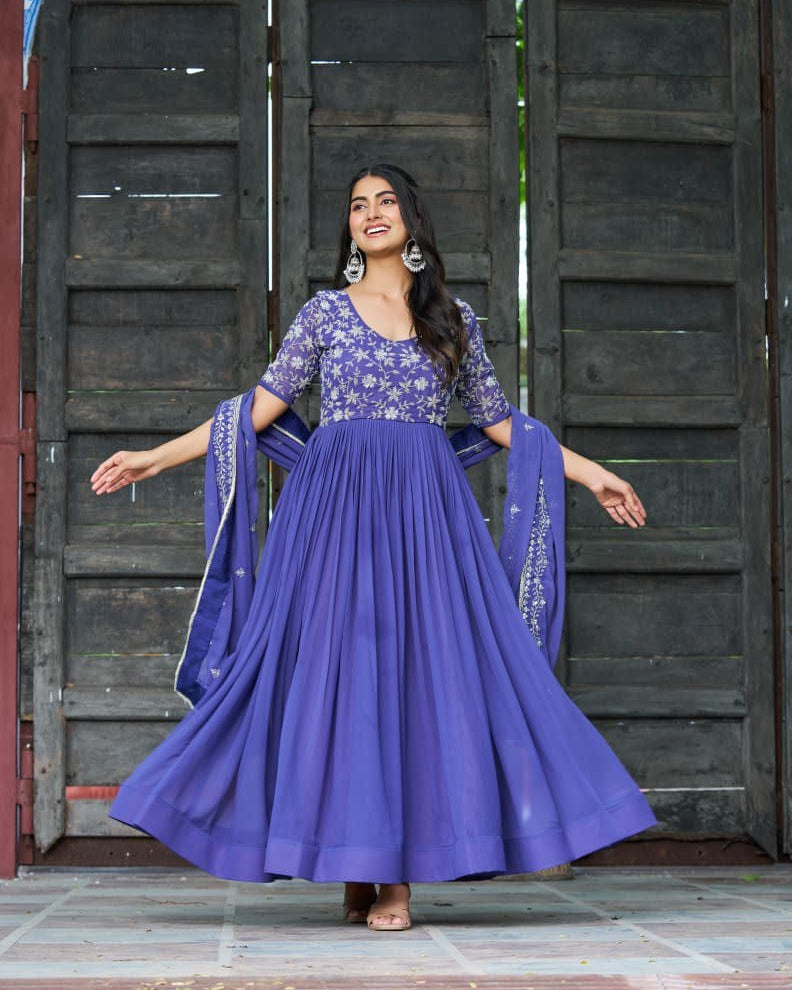 Woman in a purple traditional outfit standing in front of a wooden door.