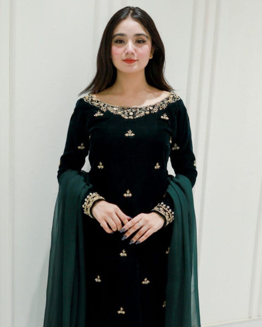Woman wearing a black traditional outfit with gold embroidery against a white paneled wall.