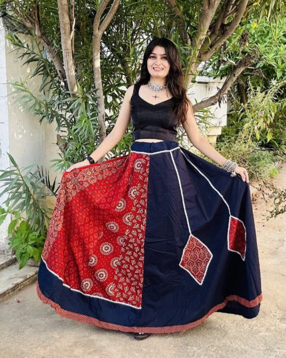Woman wearing a red and navy blue traditional outfit with a patterned skirt in an outdoor setting.