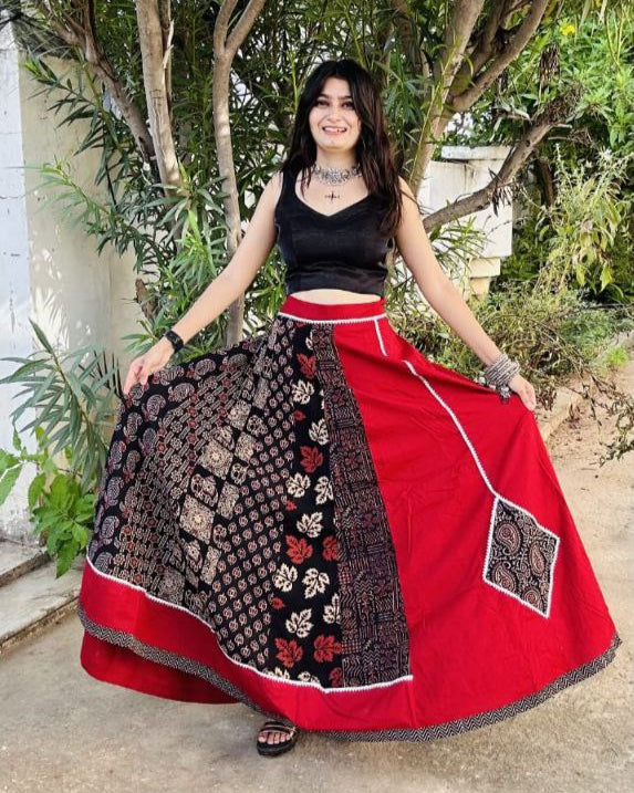 Woman wearing a red and black traditional outfit with a patterned skirt outdoors.