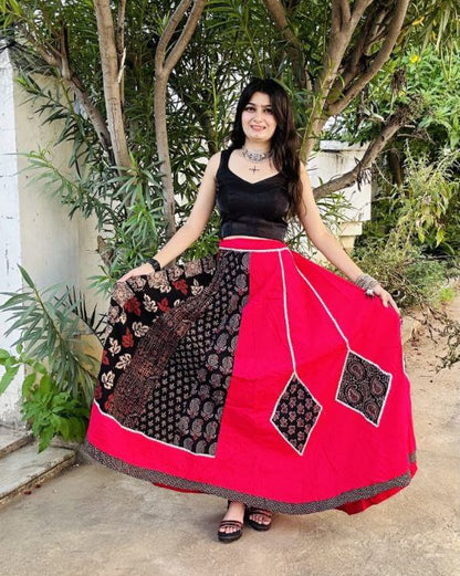 Woman wearing a red and black traditional outfit standing outdoors with trees in the background