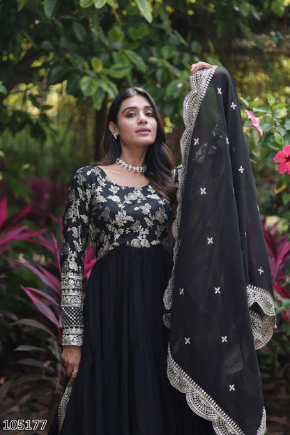 Woman holding a black embroidered dupatta against a green leafy background