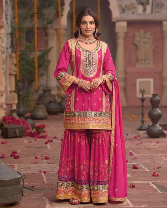 Woman in a traditional pink and gold outfit standing in an outdoor setting with decorative elements.