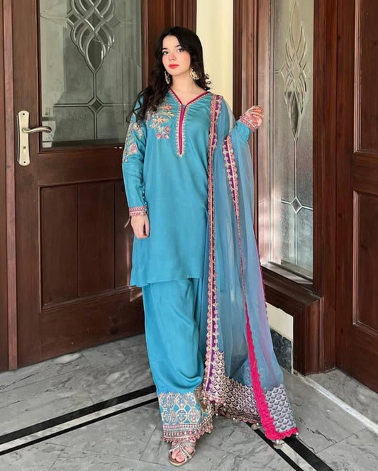 Woman in a blue traditional outfit standing in front of a wooden door.