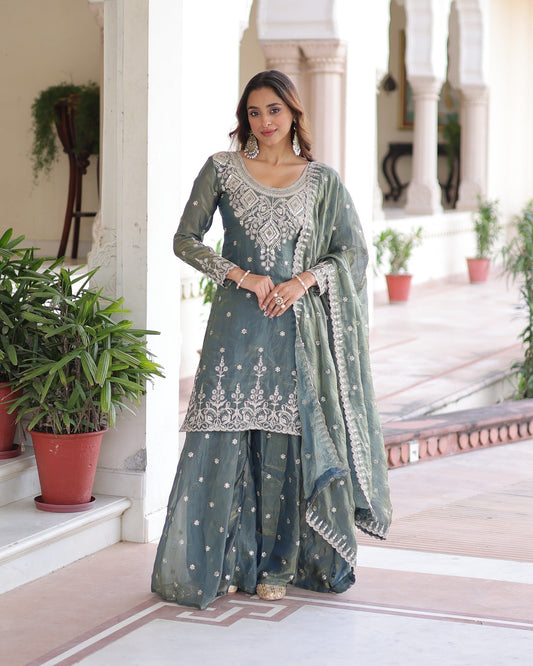 Woman in a traditional green and white outfit standing in an elegant indoor setting with plants.