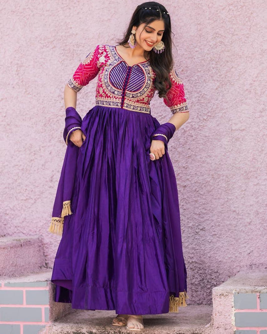 Woman in a purple and pink traditional outfit standing on stone steps with a light pink wall background.