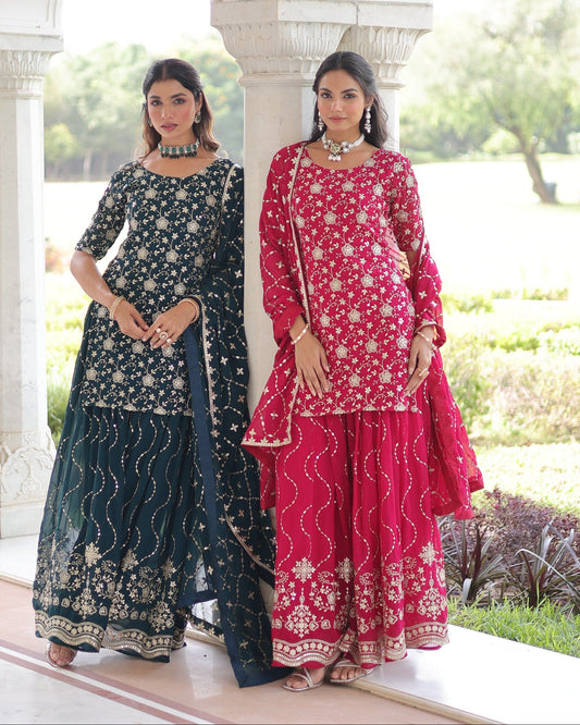 Two women in traditional outfits standing outdoors with a white architectural structure in the background.
