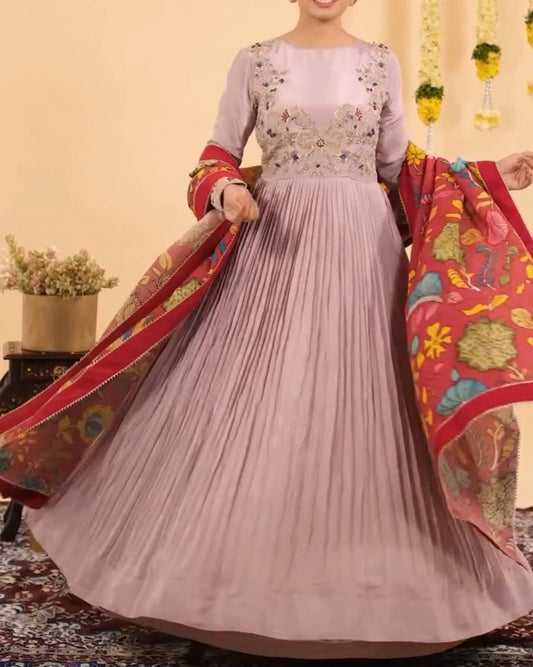 Woman in a light pink anarkali suit with floral patterns holding a colorful dupatta against a beige background.