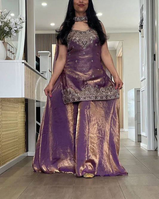 Person wearing a purple and gold traditional outfit in a room.