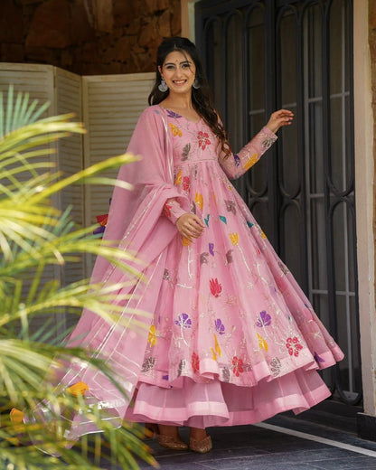 Woman in a pink traditional outfit with floral patterns standing outdoors.