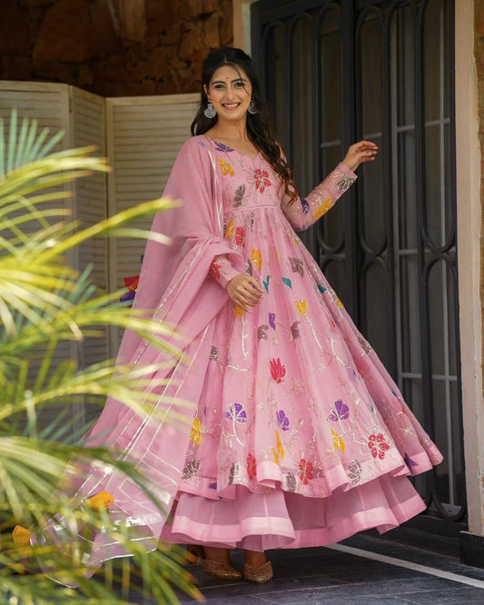 Woman in a pink traditional outfit with floral patterns standing outdoors.