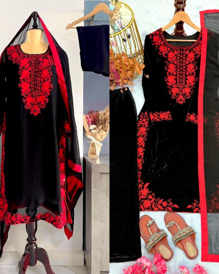 Black and red embroidered dress with matching dupatta on a mannequin and hanger, with sandals and floral decorations in the background.