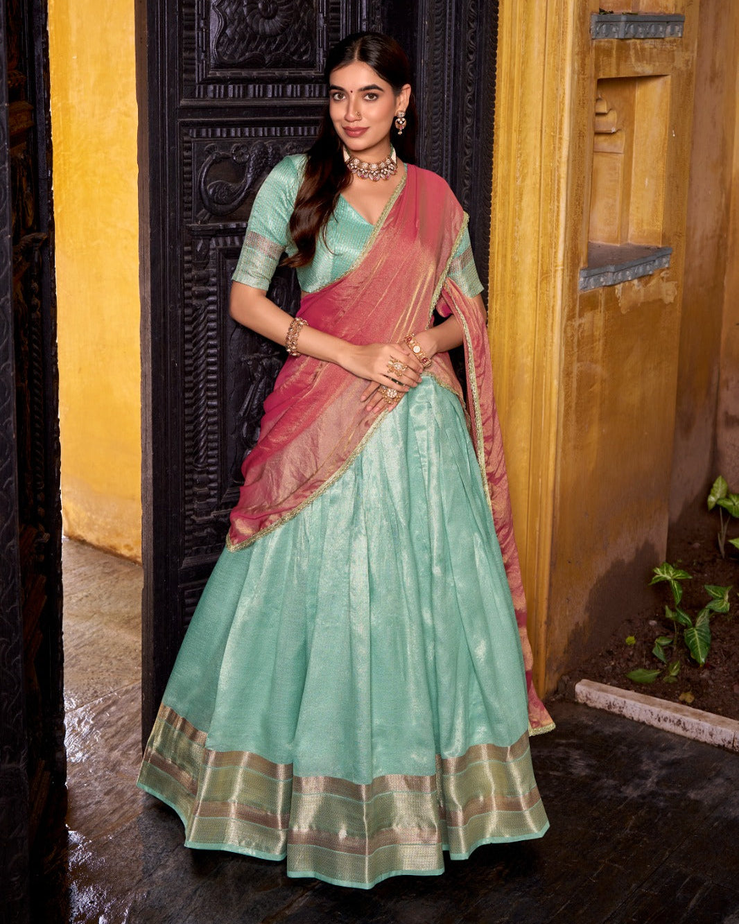 Woman in a traditional saree standing in front of a wooden door.