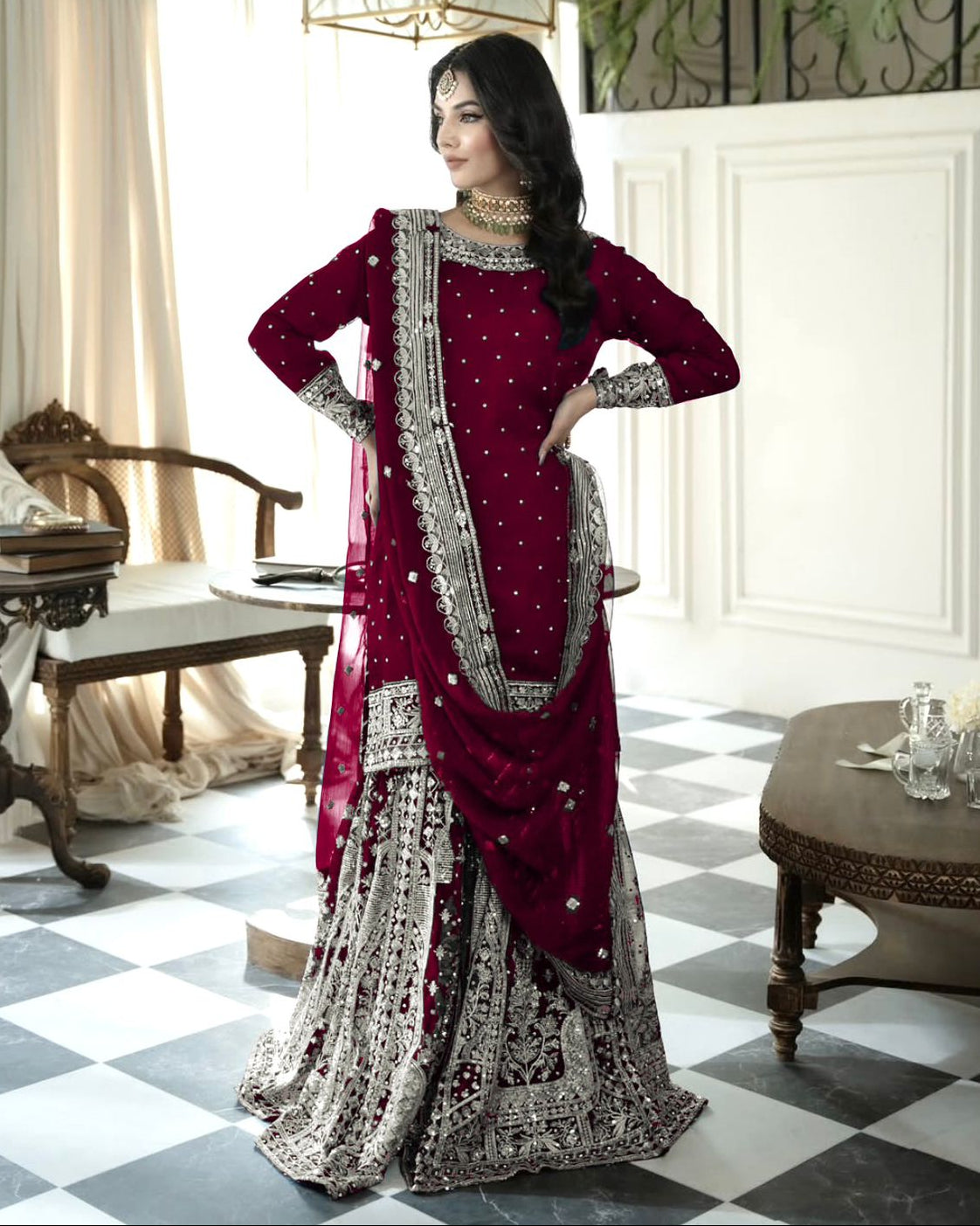 Woman in a red and silver traditional outfit standing in an elegant room with checkered floor and decorative elements.