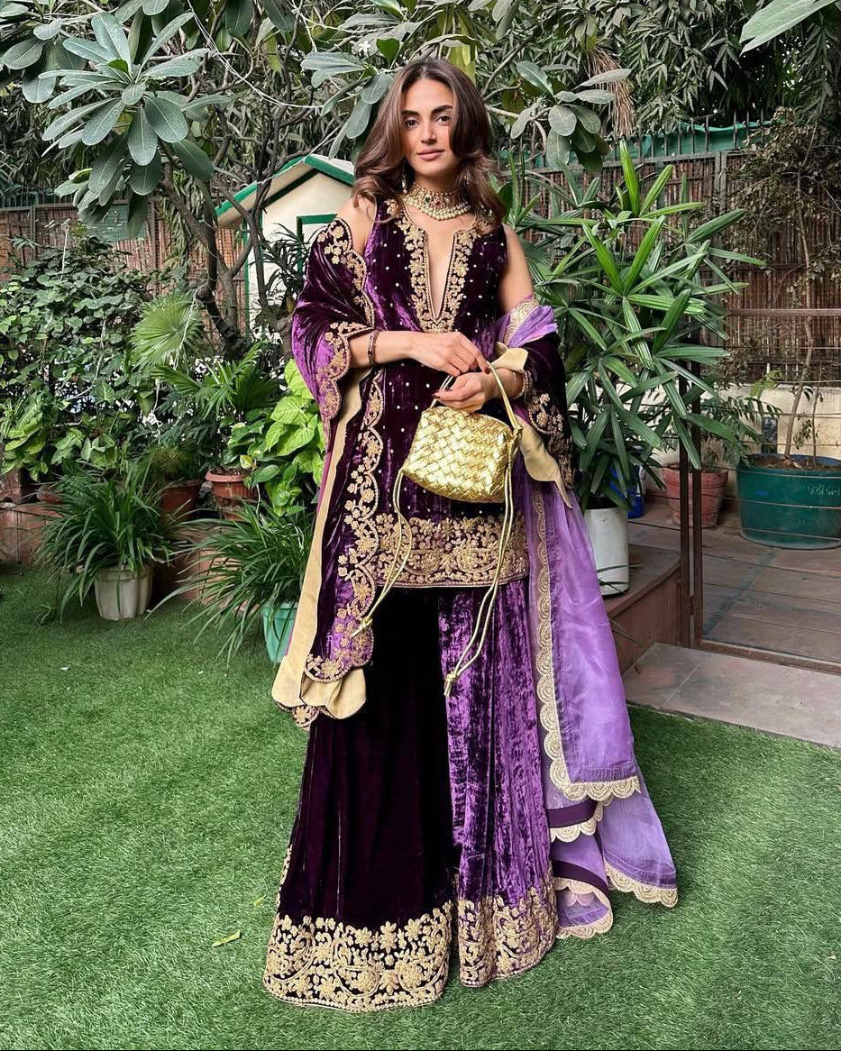 Woman in a purple and gold traditional outfit standing in a garden.