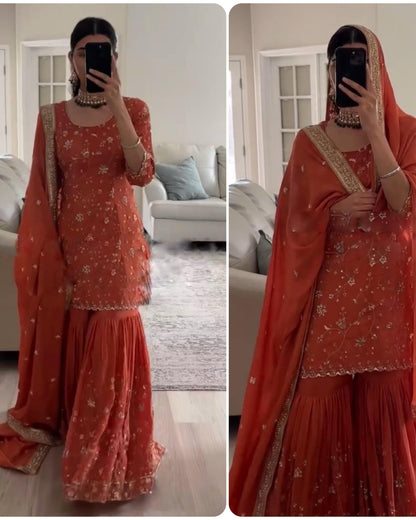 Person wearing an orange traditional outfit with floral patterns in a living room setting.