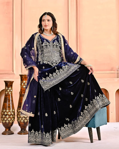 Woman in a traditional embroidered outfit sitting on a chair against a pink wall.