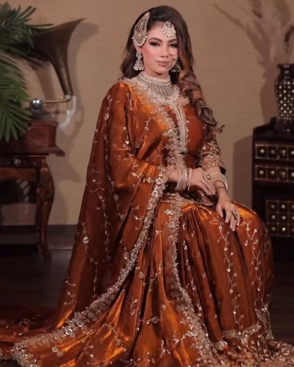 Woman in a traditional brown and gold outfit with intricate designs, sitting indoors.