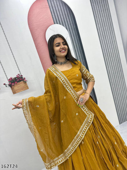 Woman in a mustard yellow traditional outfit with gold embroidery against a white background