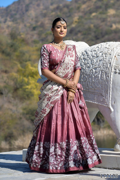 Woman in traditional pink and white saree standing next to a stone elephant sculpture with a mountainous background.