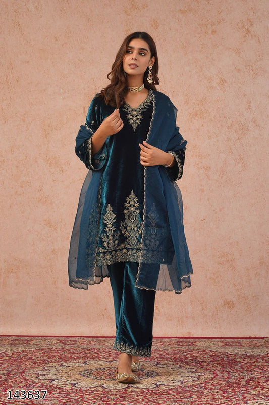 Woman wearing a teal embroidered outfit with a matching shawl against a pink background