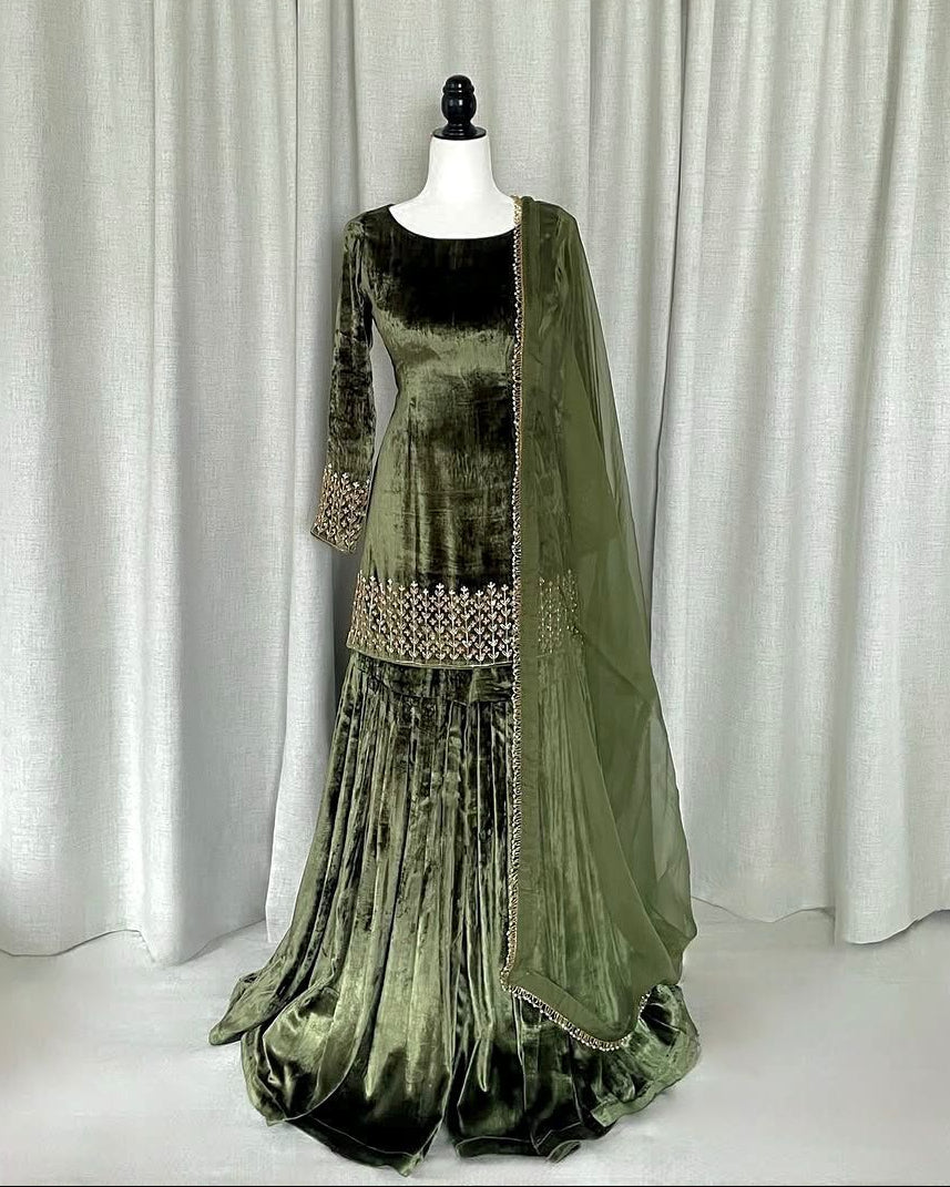 Green velvet dress with embellishments on a mannequin against a white curtain background