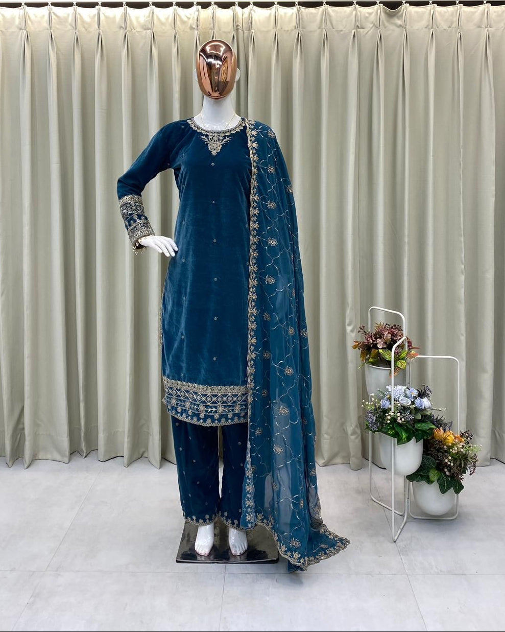 Mannequin wearing a blue traditional outfit with a dupatta against a beige curtain background.
