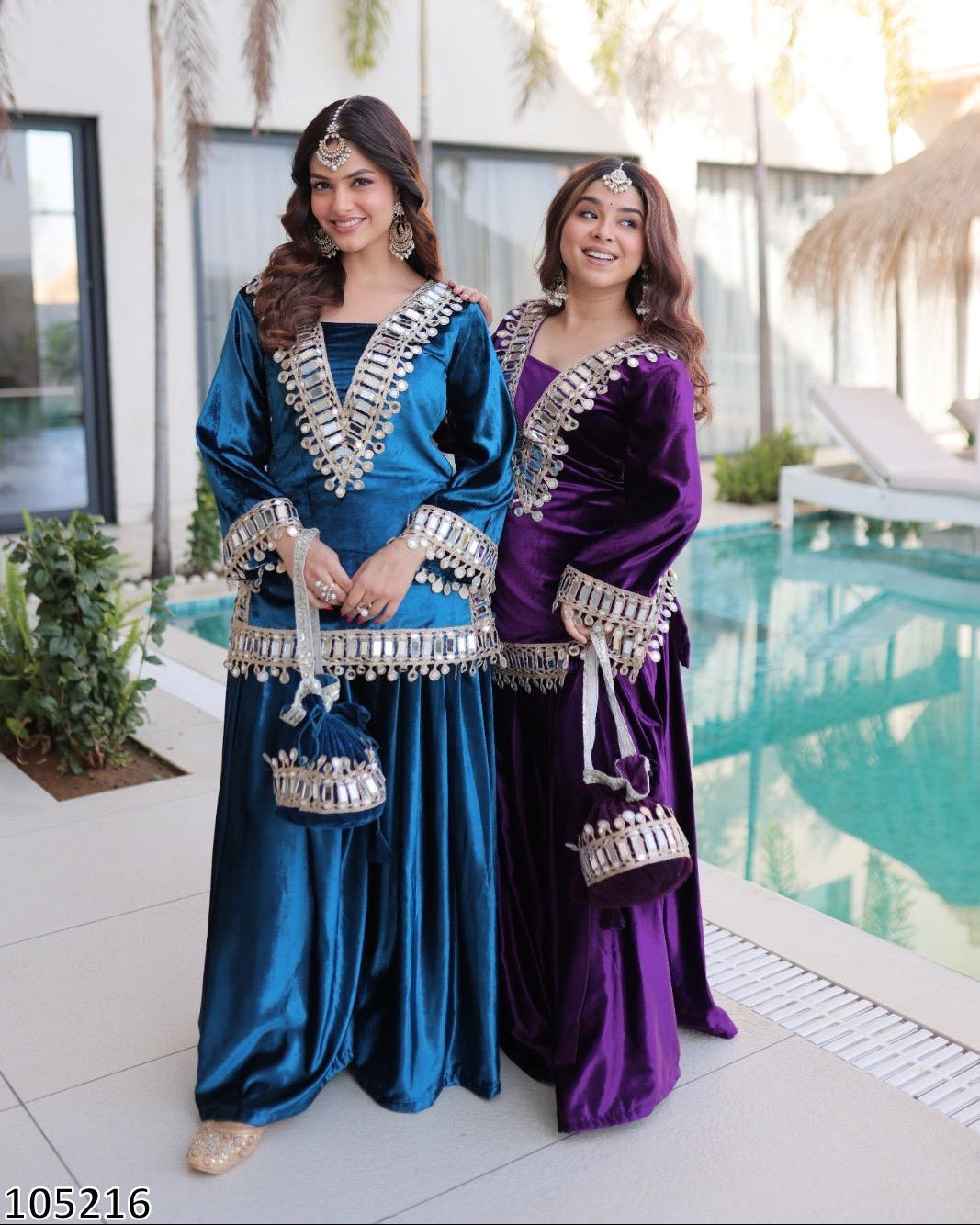 Two women in traditional blue and purple outfits standing by a pool.