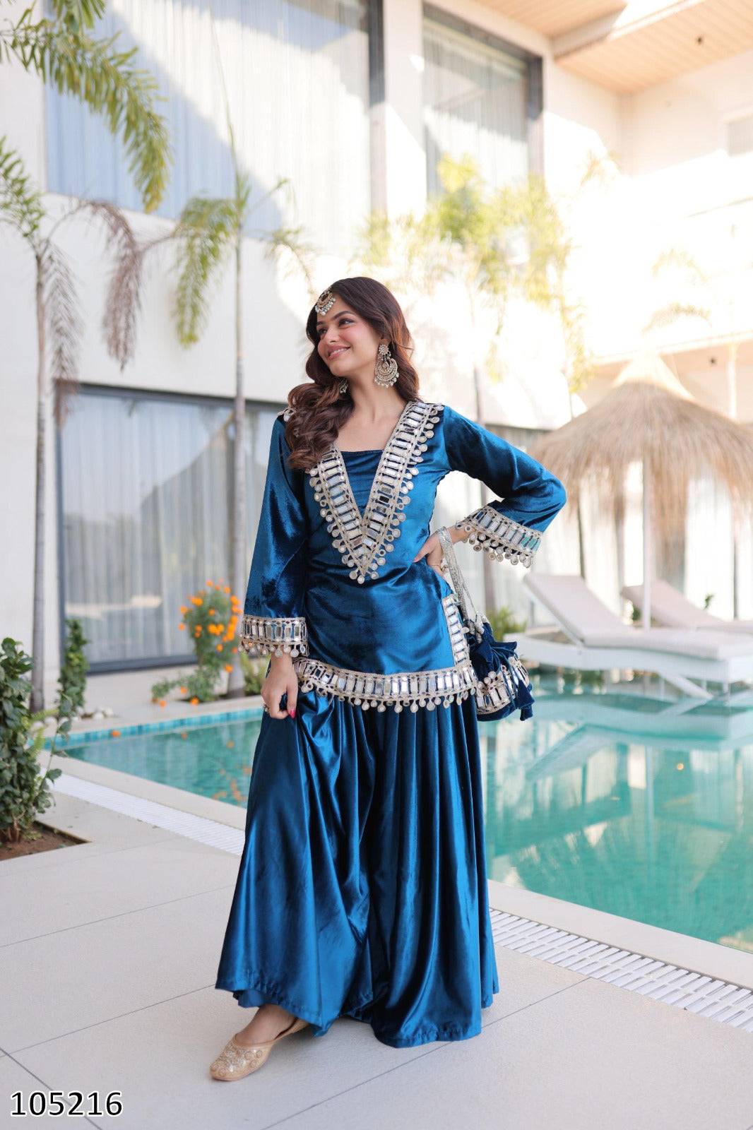 Woman in a blue traditional outfit standing by a pool with modern architecture in the background