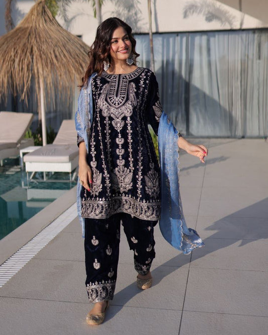 Woman in traditional black and white embroidered outfit standing by a poolside.