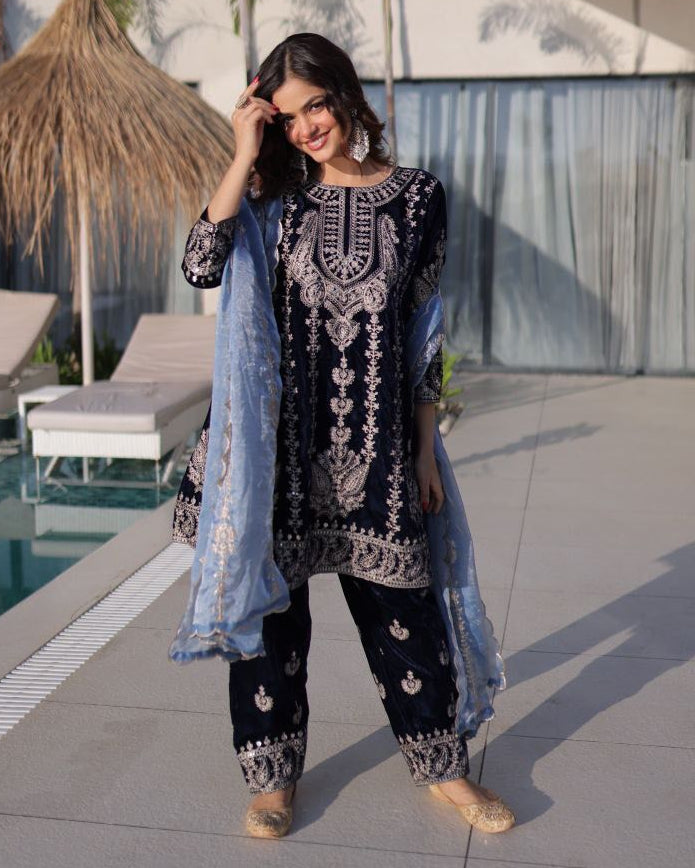 Woman in traditional black and white embroidered outfit standing by a poolside.