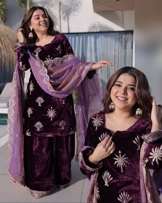 Two women in matching purple traditional outfits with white patterns, standing outdoors.