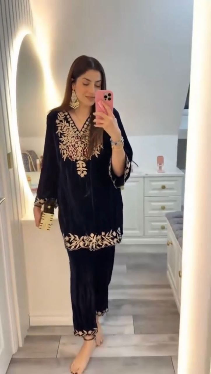 Woman wearing a black outfit with gold embroidery in a room.