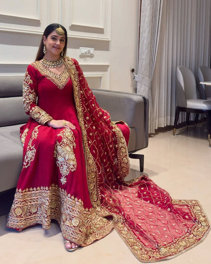 Woman in a red and gold traditional outfit sitting on a couch in a modern room.
